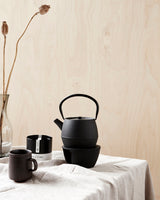 Tepotte på bord sammen med krus og the