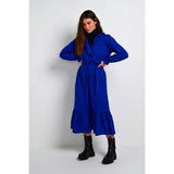 Slå-om kjole fra Kaffe i en dyb blå farve med flæser overskæringer og lange ærmer ligeledes med flæser set forfra på model