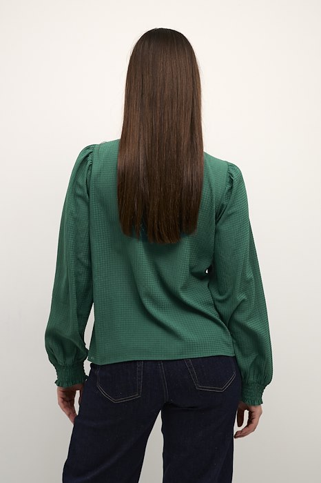 Grøn bluse med rund hals og lange ærmer som afsluttes med smock den har rund hals og slids og knap i nakken set bagfra