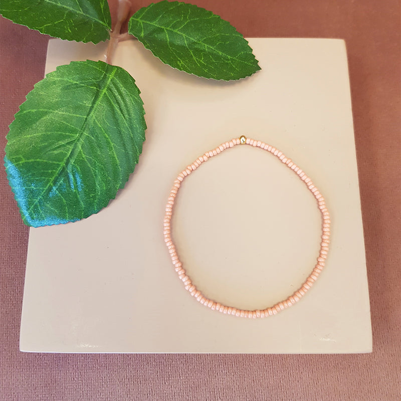 coral farvet elastikarmbånd med guld perle set oppefra