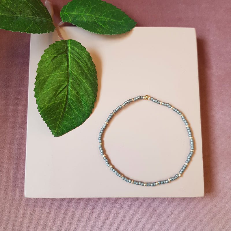 gråt elastik armbånd med guld perler set oppefra