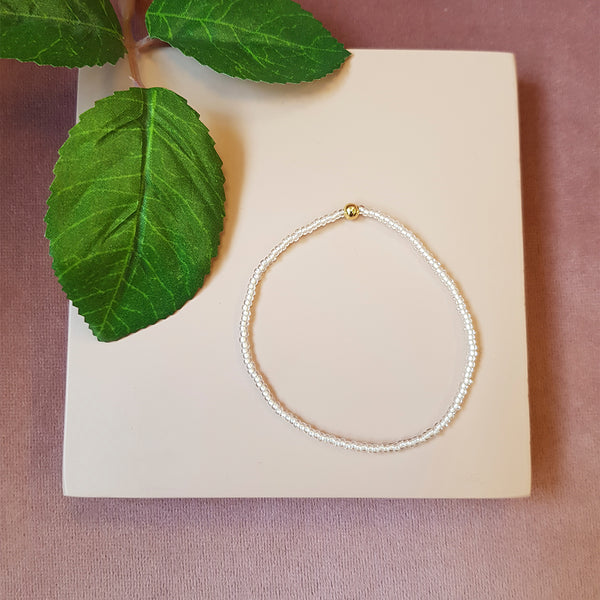 lys rosa farvet elastik armbånd med guld perle set oppefra
