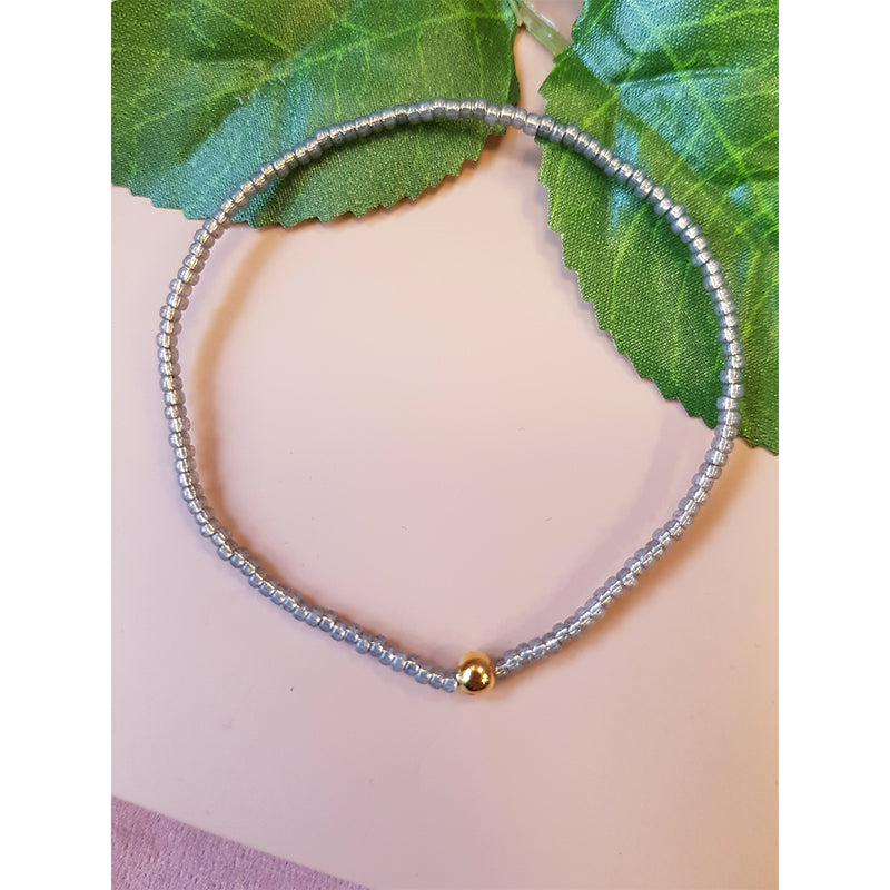 elastik armbånd med små grå perler og stor guld perle set liggende
