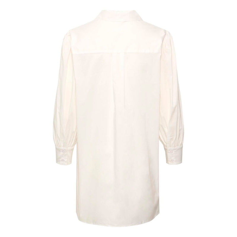 Lang hvid skjorte med flæser ned fortil den er gennemknapper har lange ærmer med fast manchet og skjortekrave set bagfra hvor man kan se overskæring på ryg samt læg