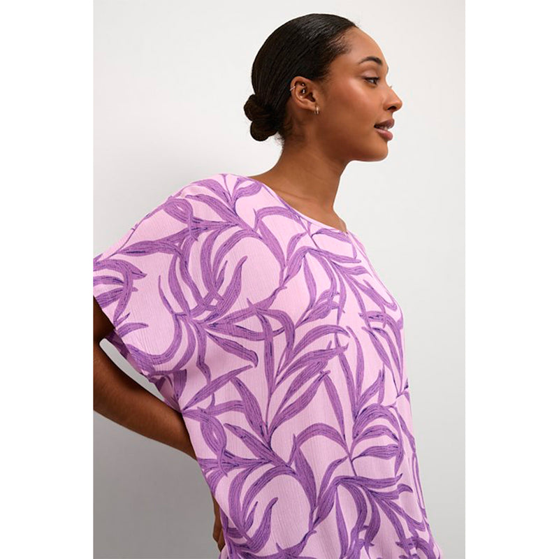 Lyselilla bluse med mørkelilla print den har rund hals og korte ærmer samt elastik i bunden set tæt på kaffe model fra siden