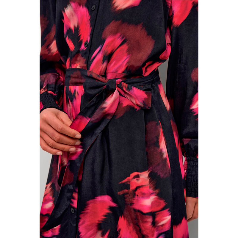 Smuk sortgennemknappet kjole med bindebånd og blomsterprint i rødlige toner den har lange ærmet med smock og skjortekrave set tæt på bindebånd