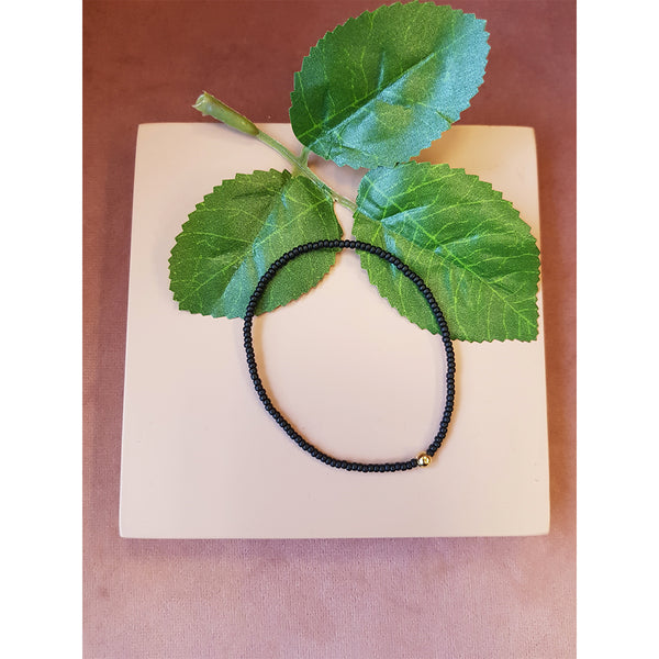 Elastik armbånd med små sorte perler og en stor guld perle set forfra