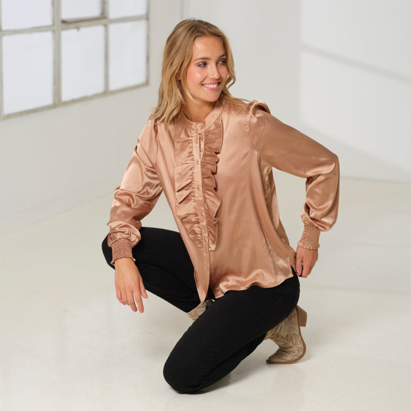 Flødefarvet shiny bluse med masser af shine og flæser ned fortil samt guld knapper den har lange ærmer med smock og rund hals set fra siden på prepair model