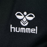 Sort Hummel træningsjakke med klassiske Hummel vinkler ned langes ærmerne og logo ved bryst den har lynlås og ribkanter set tæt på logo